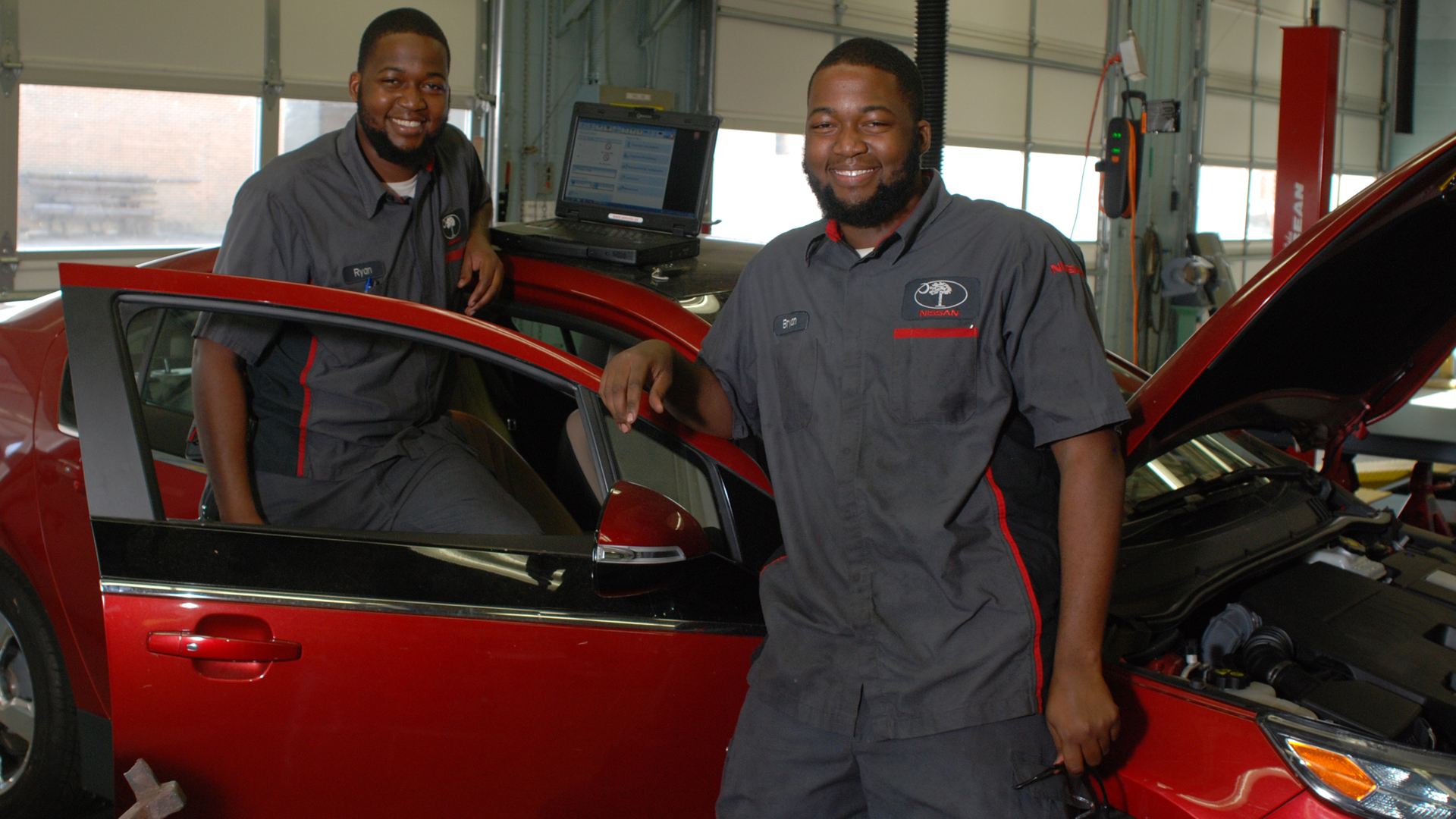  Two auto techs smiling in garage leaning on car