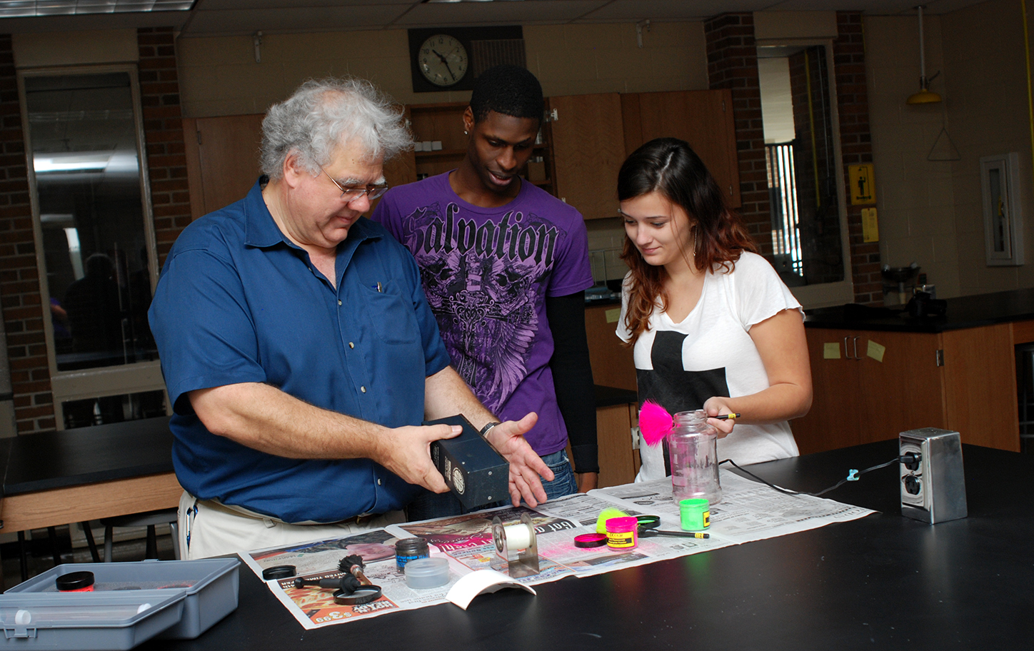 Photo of instructor with black male and white female student looking at forensic tools on a table